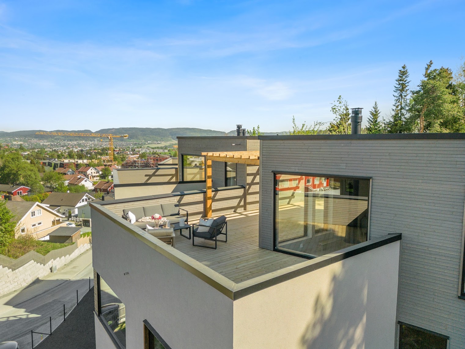 Moderne takterrasse med trepaviljong, møbler og utsikt over by og fjell.